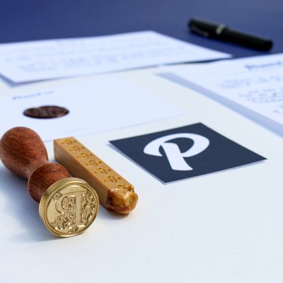 A custom gold wax seal made from the Penned logo, shown with its laser-engraved die and the Penned brand mark